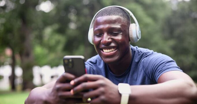 Fitness, smartphone and happy man with headphones at park on break for streaming music at garden in summer. Sports, phone or African person listening to radio, typing or laugh at meme on social media