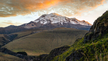 High Andes view of the north face of the Chimborazo volcano at dawn with its summit and the clouds above illuminated by the orange light of the sunrise