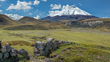 Cotopaxi volcano view from the hill of the Pucara Del Salitre Incan ruins with a clear blue sky and the remains of a stone wall in the foreground