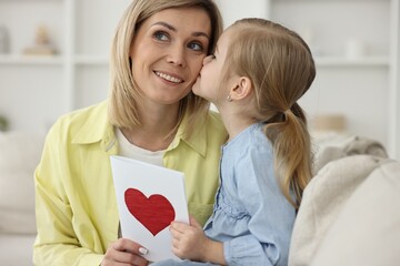 Little daughter kissing and congratulating her mom with greeting card at home. Happy Mother's Day