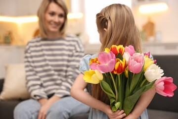 Little girl hiding bouquet of tulips for mom at home, selective focus. Happy Mother's Day