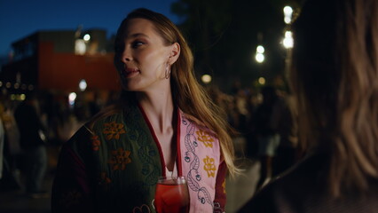 Obraz premium Woman holding cocktail talking with friends at night city party outdoors closeup