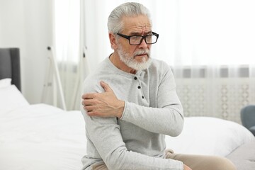 Arthritis symptoms. Man suffering from pain in shoulder on bed at home