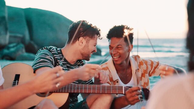 Friends, laughing together and sparkler on beach, guitar for music and fun outdoor at reunion. Firework, celebration and happy in nature, people at social gathering for freedom and party by the ocean