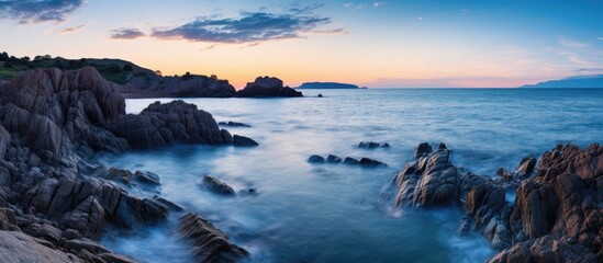 Fototapeta na wymiar A breathtaking long exposure photo capturing the rocky shoreline at dusk, with the oceans waves crashing against the rocks under the colorful sky