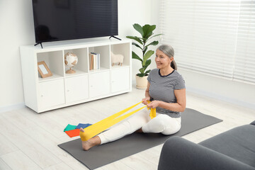 Senior woman doing exercise with fitness elastic band on mat at home