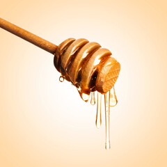 Natural honey dripping from dipper on pale orange background