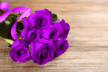 Violet roses on wooden table, space for text. Funeral attributes