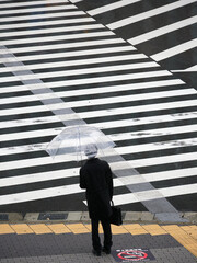 ハイアングルで撮影した雨の日の都市の交差点の横断歩道で信号待ちのサラリーマンの姿
