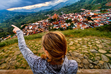 Woman points out the town of Jerico (Colombia) from a hill at sunset
