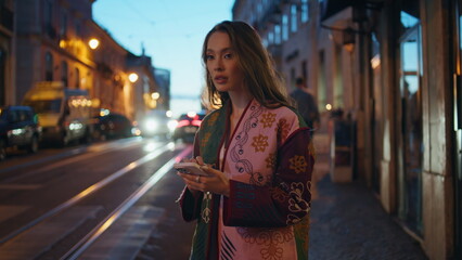 Fototapeta premium Woman hailing taxi evening downtown street holding smartphone. Girl catching cab