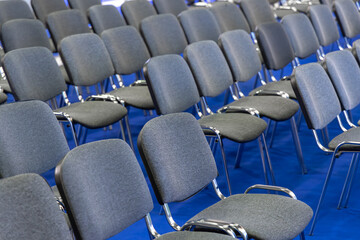Perfectly Aligned Grey Chairs on Blue Carpet for Seminars. Contemporary Grey Seating Arrangement for Corporate Conferences. Ready for Attendees: Sleek Chair Setup in a Business Event Hall