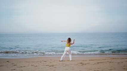 Flexible girl dancer bending body performing dance on evening sea coast. 