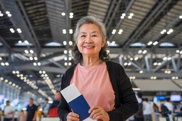 happy asian senior woman with grey hair holding passport and boarding pass in the airport,concept of elderly retired people lifestyle,travel,wellness,wellbeing