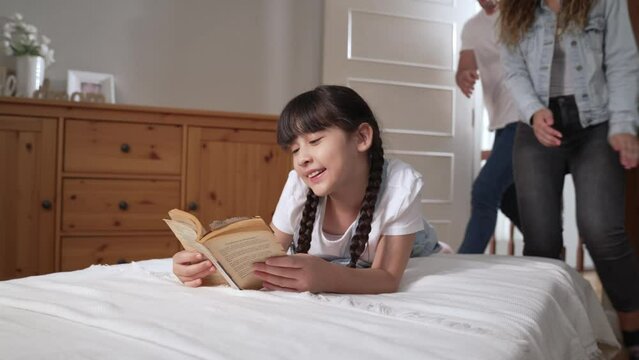 Happy modern family wakes up their little girl on the weekend with playful tickle expressing their love and affection for their young daughter, laughing and smiling together. Fastidious