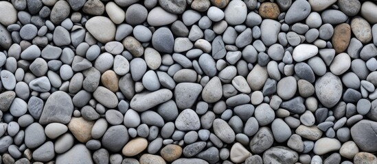 A stack of bedrock rocks creates a unique pattern on the beach resembling a cobblestone road surface, with smaller pebbles and gravel surrounding it - obrazy, fototapety, plakaty