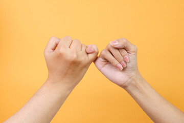 Male and female hands hook each other little finger pinkie as a symbol of promise or pardon isolated on yellow background. Together and relationship concept - obrazy, fototapety, plakaty