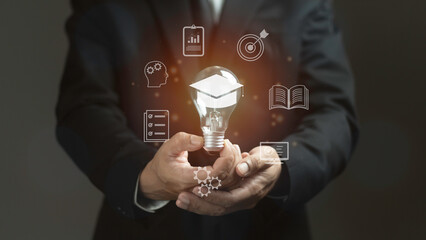 A man is holding a light bulb with a graduation cap on it