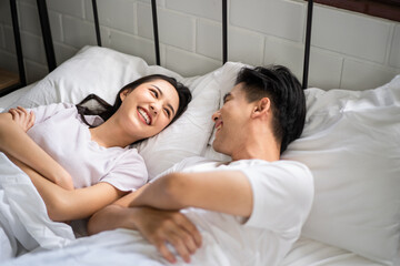 Asian new marriage couple lying down on bed and looking at each other. 