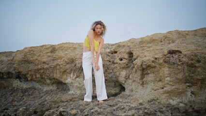 Naklejka premium Curly girl performer dancing on sandy rock at summer evening. Woman moving body