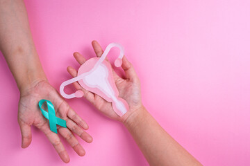 Top View of Female Hands Holding Teal Ribbon and Uterus Cutout. Ovarian cancer and Gynecological...