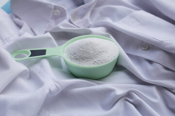 Detergent powder in measuring spoon on cloth before washing. Laundry concept.