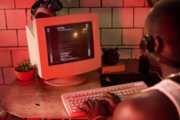 Selective focus over shoulder shot of unrecognizable Black man hacking database using old desktop...
