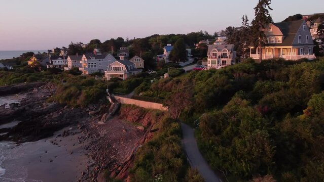 Aerial sunset of Ogunquit Maine USA drone fly above waterfront house luxury resort revealing Marginal way trail path on Atlantic Ocean coastline 
