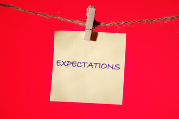 Word Expectations written on a yellow sticker on a rope with a clothespin on a red one