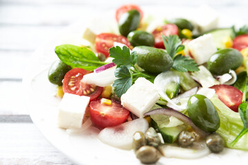 Healthy Salad with Feta Cheese, Green Olives, Baby Spinach, Cucumber, Cherry Tomatoes and Capers. Bright background. Close up.	