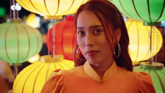 Slow motion portrait close up of Vietnamese woman in traditional yellow dress with lantern lights with direct eyeline