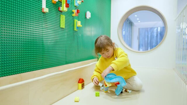 Little Adorable Cute Caucasian American Girl Playing With Colorful Blocks Building Ramp Bringe At Indoor Playroom Sitting on a Floor - slow motion wide