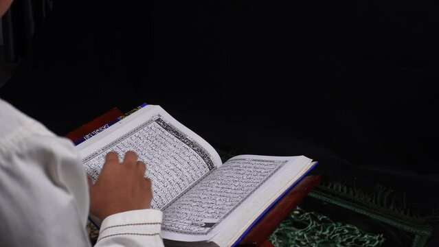 person reading holy quran on mini wooden table with isolated dark background