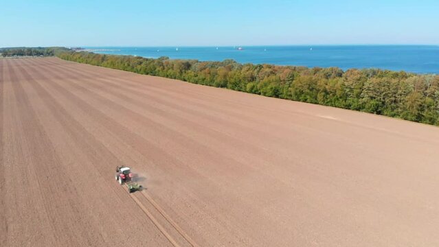 Aerial: tractor plowing the field by the sea in Northern Germany in a sunny day