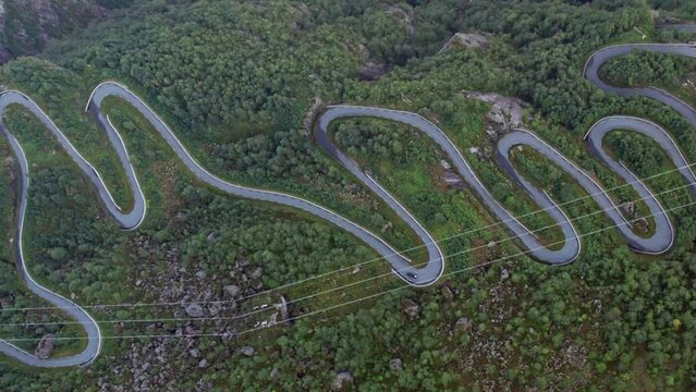Close aerial top down view of a tight twisting serpentine road as it snakes up a steep, forest covered valley side, next to a Fjord in Norway.