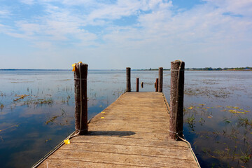 A wooden pier on a large pond with small cornices surrounding it.