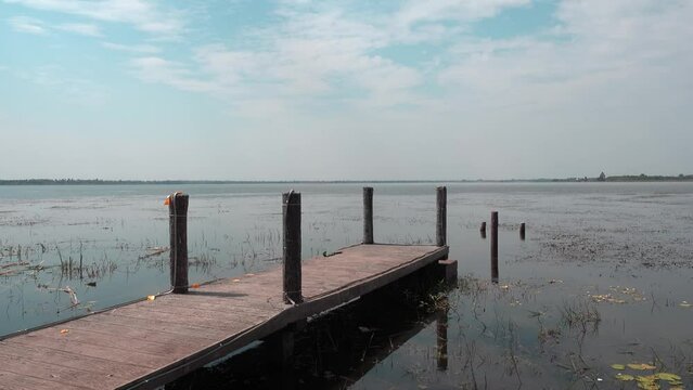 A wooden pier on a large pond with small cornices surrounding it.