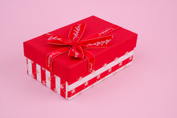 Closed red gift box with ribbon and bow on pink background.	