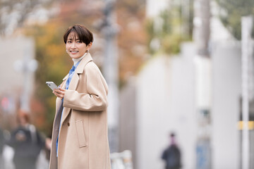 携帯電話を持ち街中を歩く女性。