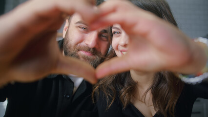 Close-up portrait of young happy couple making heart shape with joined fingers and looking at...
