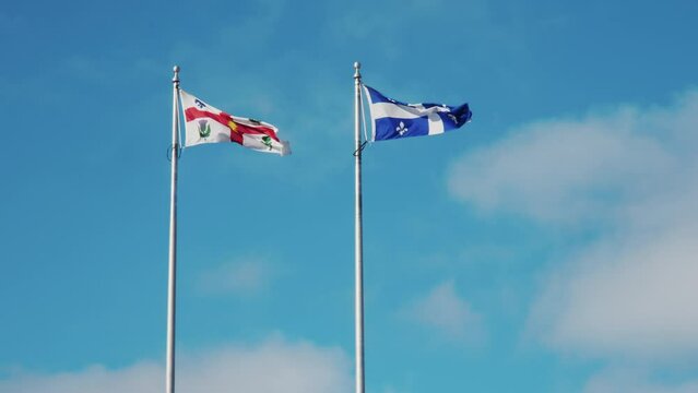 Montreal and Quebec flags flutter proudly side-by-side against a clear blue sky with wispy clouds
