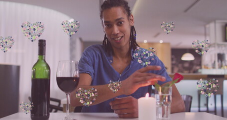 Image of heart icons over happy biracial man with wine having image call