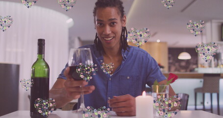 Image of heart icons over happy biracial man with wine having image call