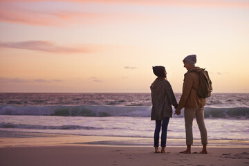 Couple, holding hands and love at sunset by water, ocean waves and peace for romance in relationship. People, back and security in marriage, sea and travel together on vacation or holiday for date