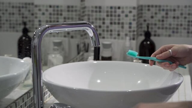 Women's hands squeeze toothpaste from a tube onto a toothbrush in the bathroom above the sink. Morning and evening treatments