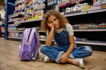 Bored or tired girl child sitting on floor of stationery shop