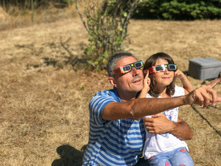 Father and daughter looking at the sun during a solar eclipse on a country park, family outdoor...