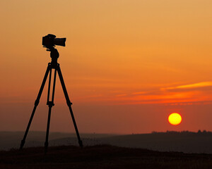 Camera tripod silhouetted against a dramatic sunset, showcasing stability for the perfect shot