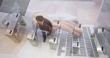 Image of hands using laptop over businessman walking through turnstiles