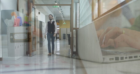 Image of hands using laptop over businessman walking in office corridor
